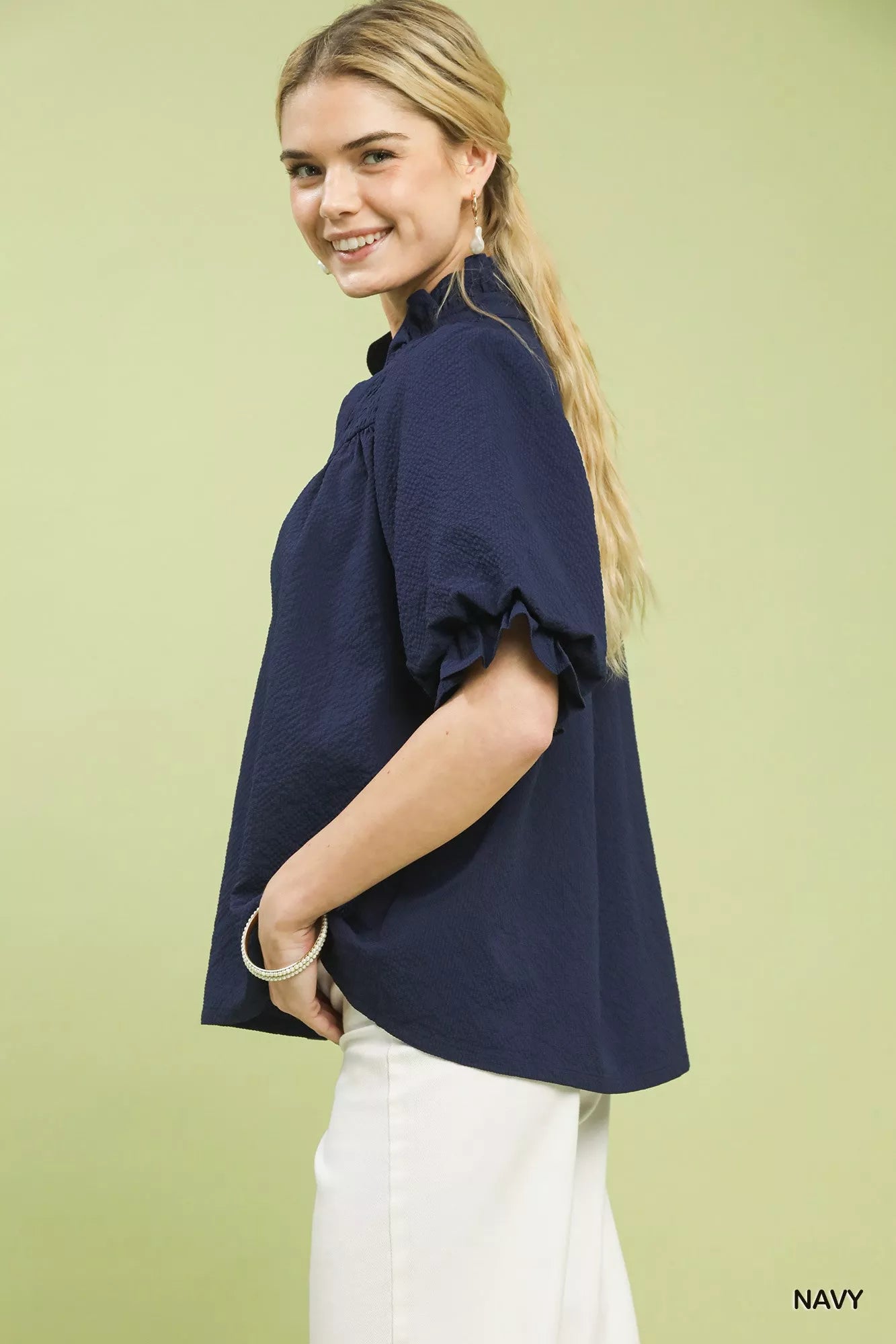 NEWYORKLISTED STYLE COLLECTION: Woman wearing a navy blue blouse with ruffled sleeves on a light green background