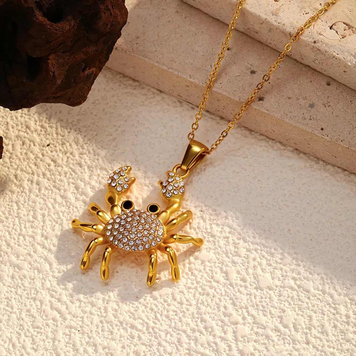 NYLD Glamour Collection by NEWYORKLISTED: Gold crab-shaped pendant with gemstones on a beige surface