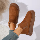 NEWYORKLISTED SHOE COLLECTION: A pair of women's brown suede slip-on ankle boots with a fuzzy lining, shown being worn with blue jeans against a bright white background with soft shadows.
