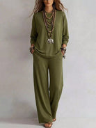 NEWYORKLISTED STYLE COLLECTION: A woman modeling a matching olive green lounge set consisting of a long-sleeve top and wide-leg pants, styled with layered necklaces and bracelets against a plain light gray background.