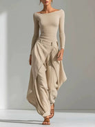 NEWYORKLISTED STYLE COLLECTION: A woman modeling a beige off-the-shoulder long-sleeve top paired with matching draped high-waisted maxi pants, styled with brown strappy sandals against a minimalist light gray studio background.
