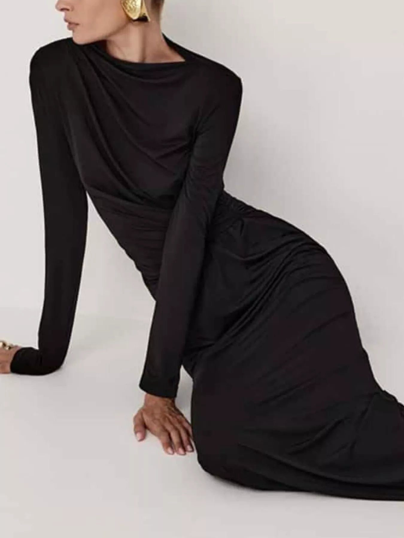 NEWYORKLISTED STYLE COLLECTION: Model is wearing a black long-sleeve dress sitting on a white floor.