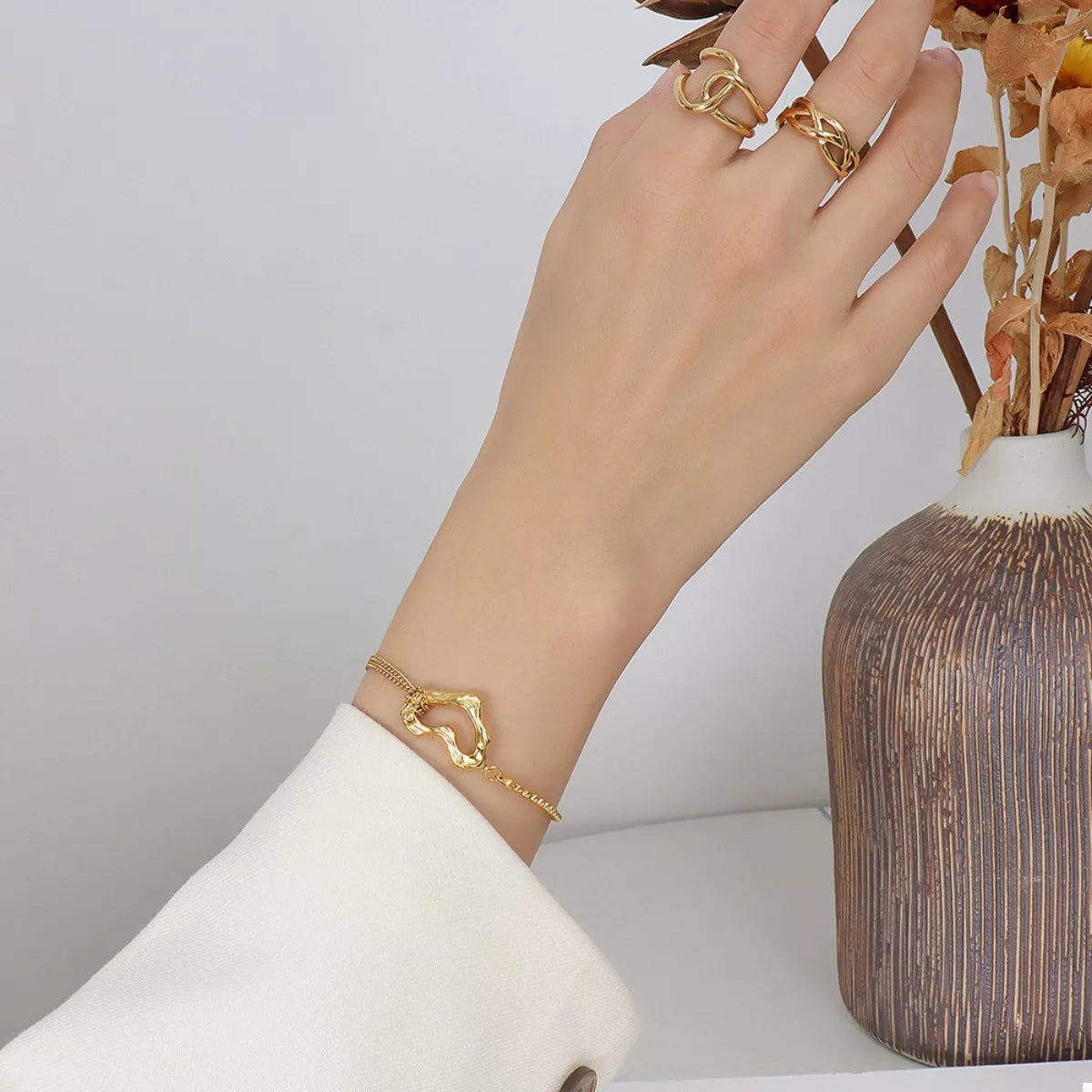 NYLD Glamour Collection by NEWYORKLISTED: Hand wearing gold jewelry with a vase in the background