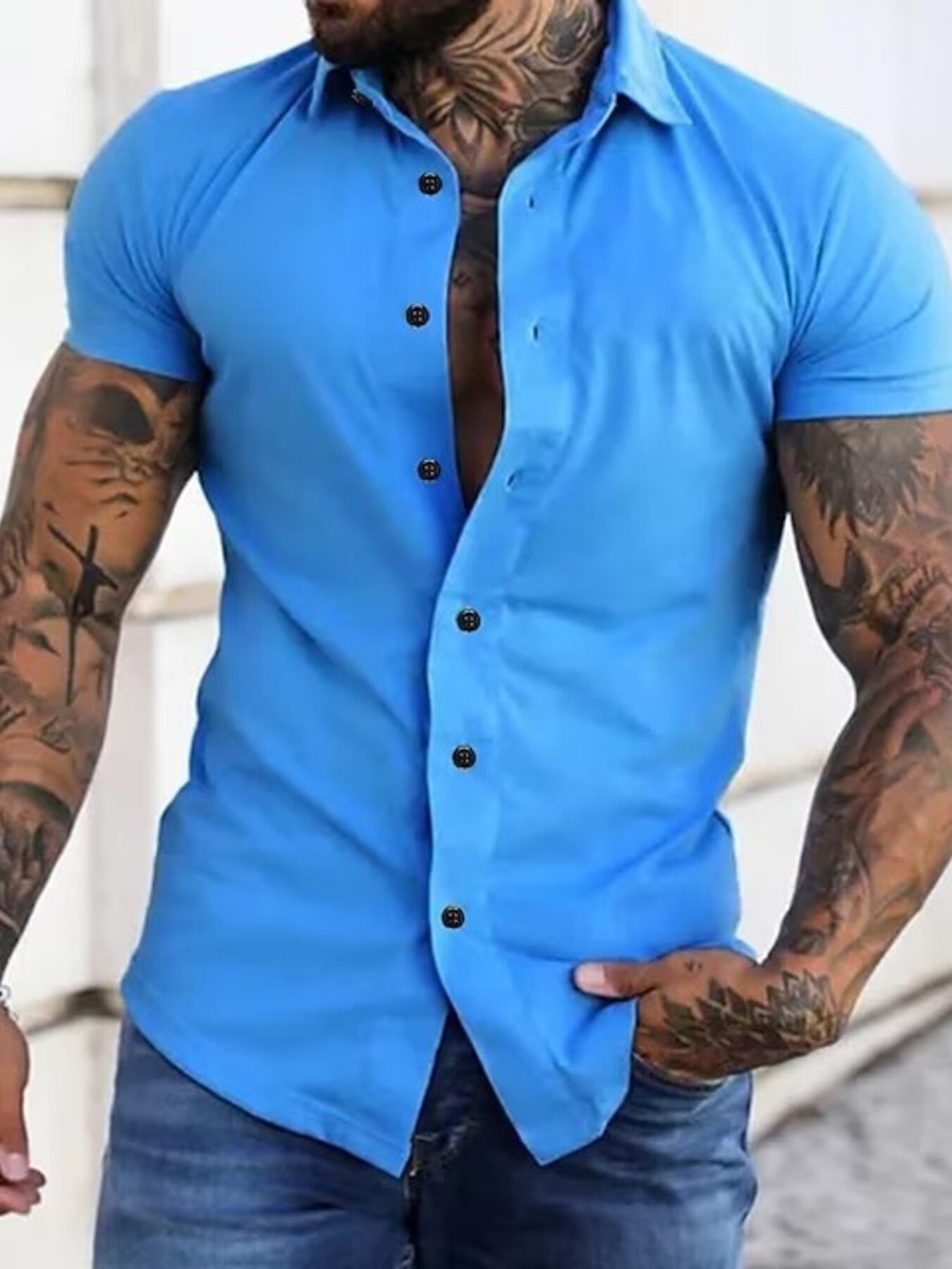 NEWYORKLISTED ATLAS MEN's COLLECTION: Man wearing a blue short-sleeve button-up shirt with tattoos on arms.