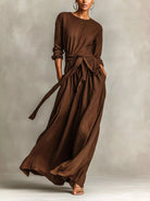 NEWYORKLISTED STYLE COLLECTION: Woman wearing a long brown dress against a neutral background