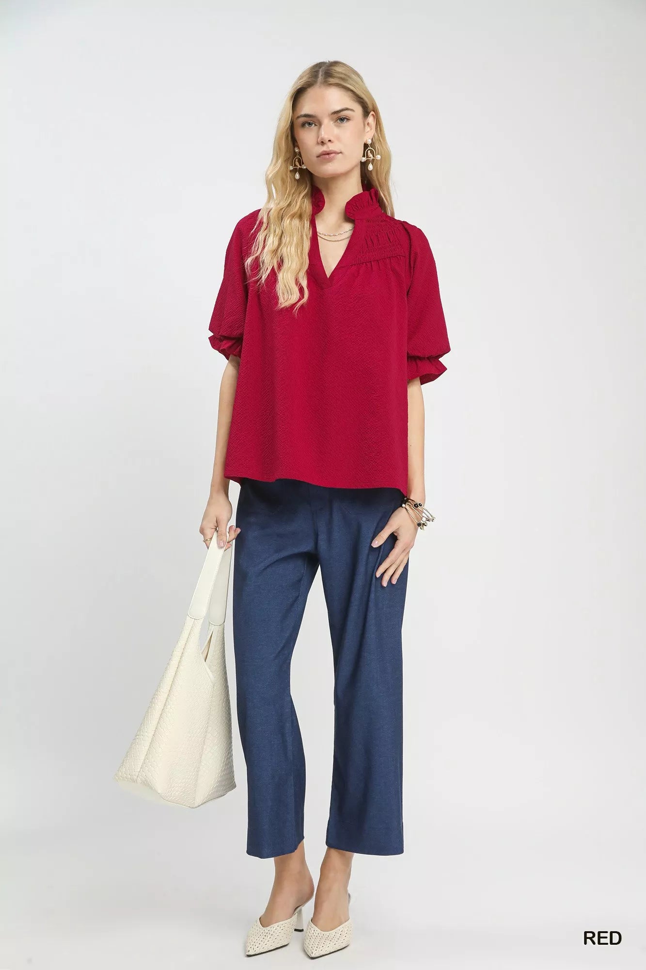 NEWYORKLISTED Style Collection: Woman wearing a red blouse and blue pants holding a white bag on a white background
