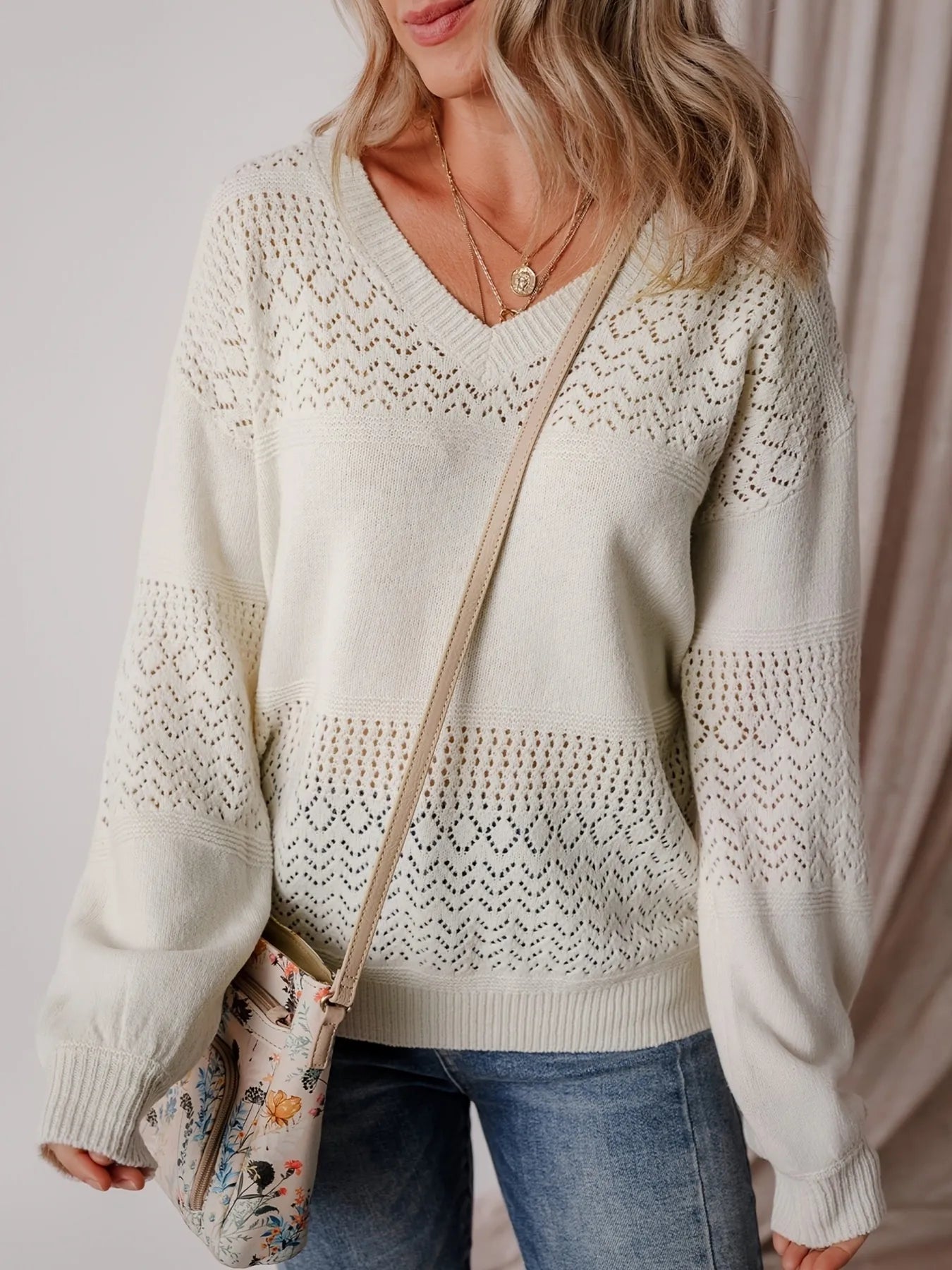 NEWYORKLISTED STYLE COLLECTION: Woman wearing a cream knitted sweater with a subtle pattern, holding a floral handbag.