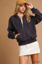 NEWYORKLISTED STYLE COLLECTION: Woman wearing a black jacket, beige cap, and white shorts on a brown background