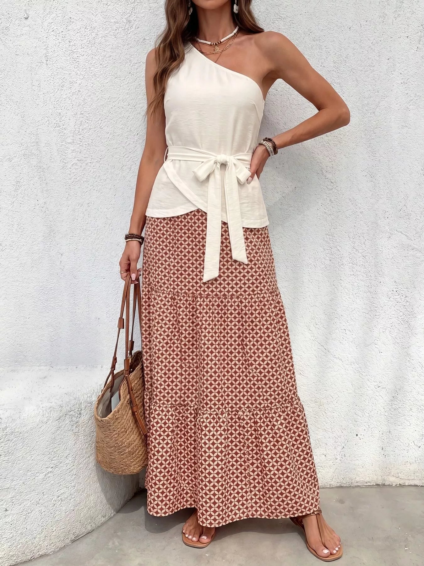NEWYORKLISTED STYLE COLLECTION: Woman wearing a white one-shoulder top and patterned skirt against a light gray wall.