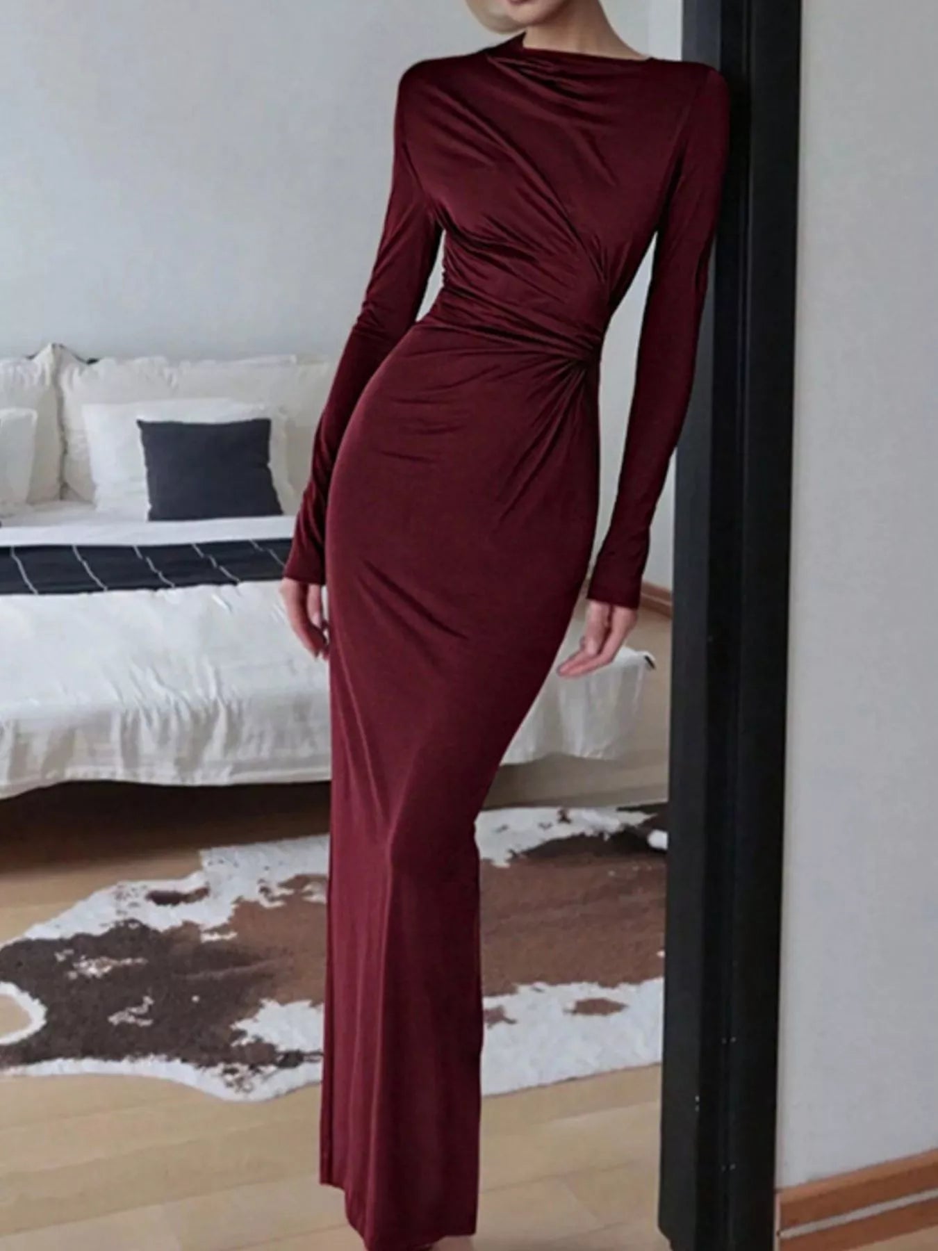 NEWYORKLISTED STYLE COLLECTION: Person wearing a burgundy dress standing in a room with a bed and cowhide rug.