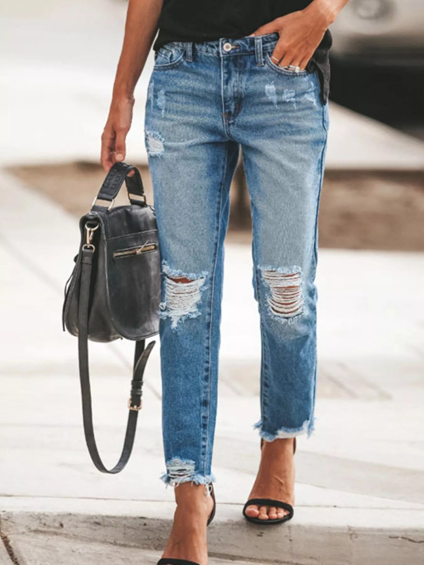 NEWYORKLISTED STYLE COLLECTION: Person wearing distressed blue jeans with a black handbag on a blurred background