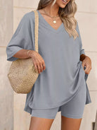 NEWYORKLISTED COMFORT COLLECTION: Woman wearing a gray outfit with a straw bag against a neutral background
