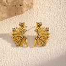 NYLD Glamour Collection by NEWYORKLISTED: Gold earrings with gemstones on a textured beige surface
