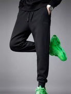 NEWYORKLISTED ATLAS MEN's COLLECTION: Person wearing black jogger pants and green sneakers on a gray background