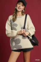 NEWYORKLISTED STYLE COLLECTION: Woman wearing a cream sweater with gray floral patterns on a red background