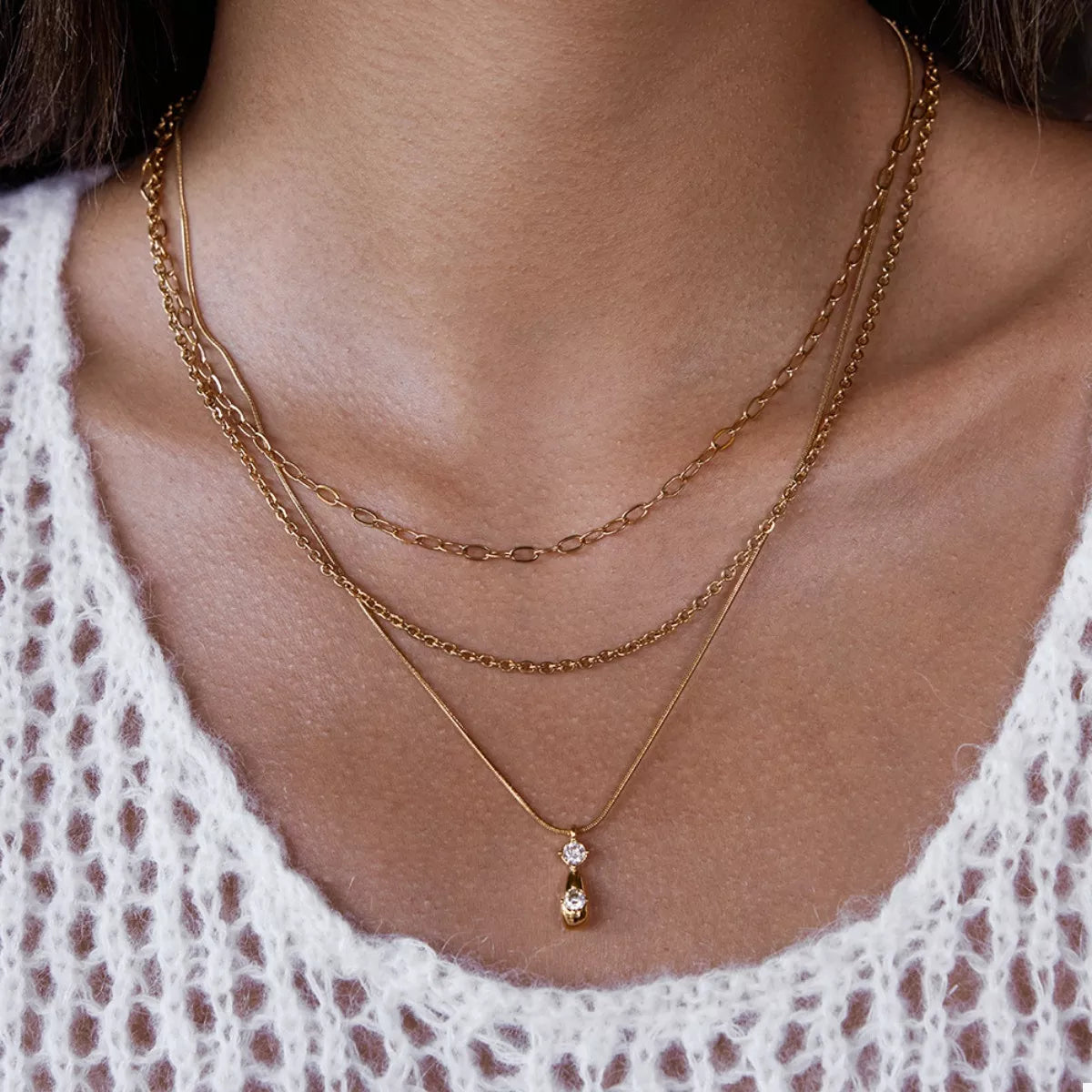 NYLD Glamour Collection by NEWYORKLISTED: Close-up of a person wearing a gold necklace with a pendant, layered with another necklace.
