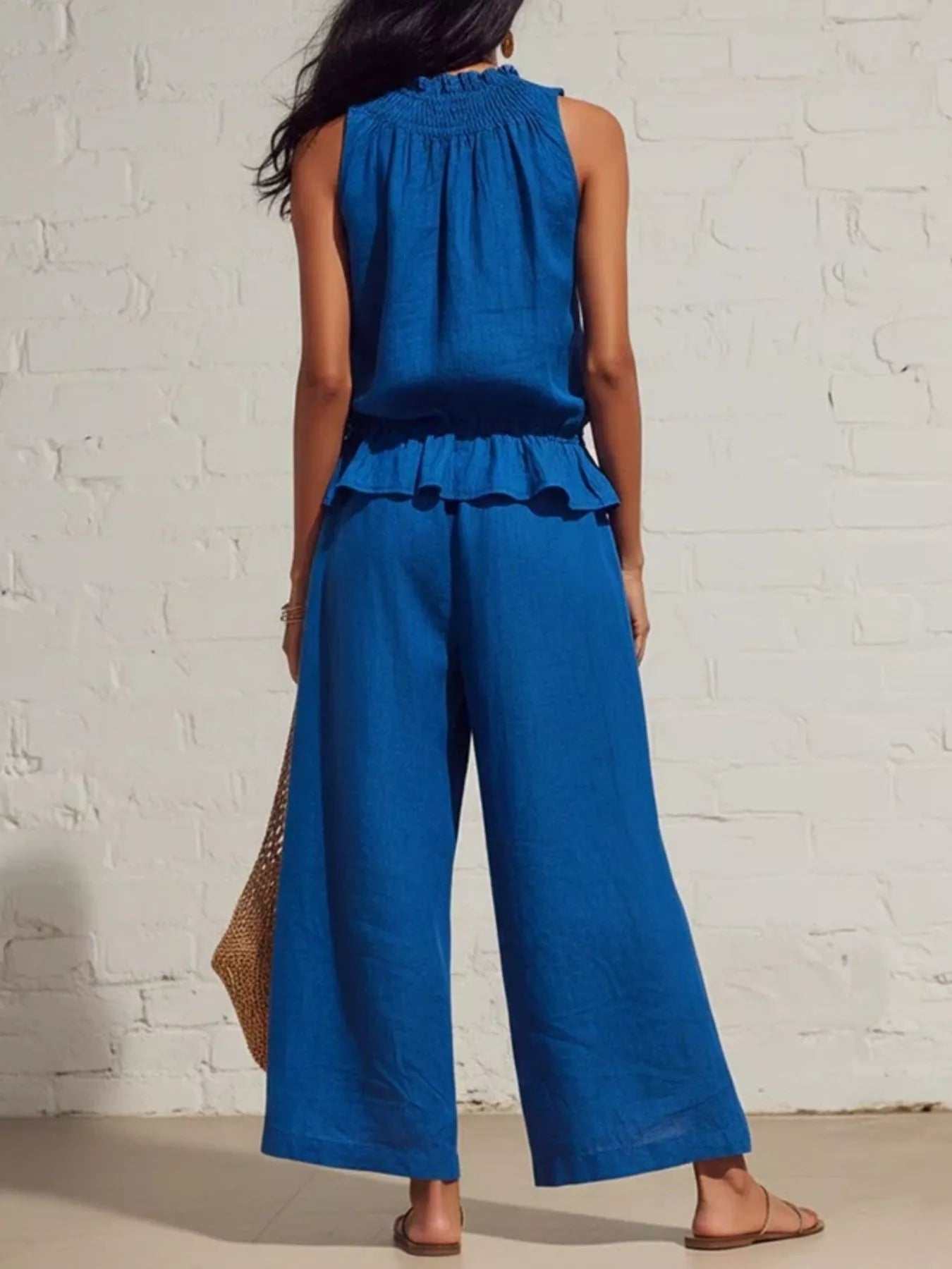 NEWYORKLISTED STYLE COLLECTION: Woman wearing a blue jumpsuit against a white brick wall.