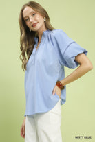 NEWYORKLISTED STYLE COLLECTION: Woman wearing a light blue blouse with short sleeves on a light green background