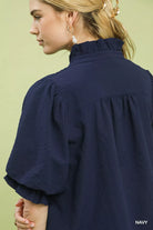 NEWYORKLISTED STYLE COLLECTION: Woman wearing a navy blue blouse against a light green background