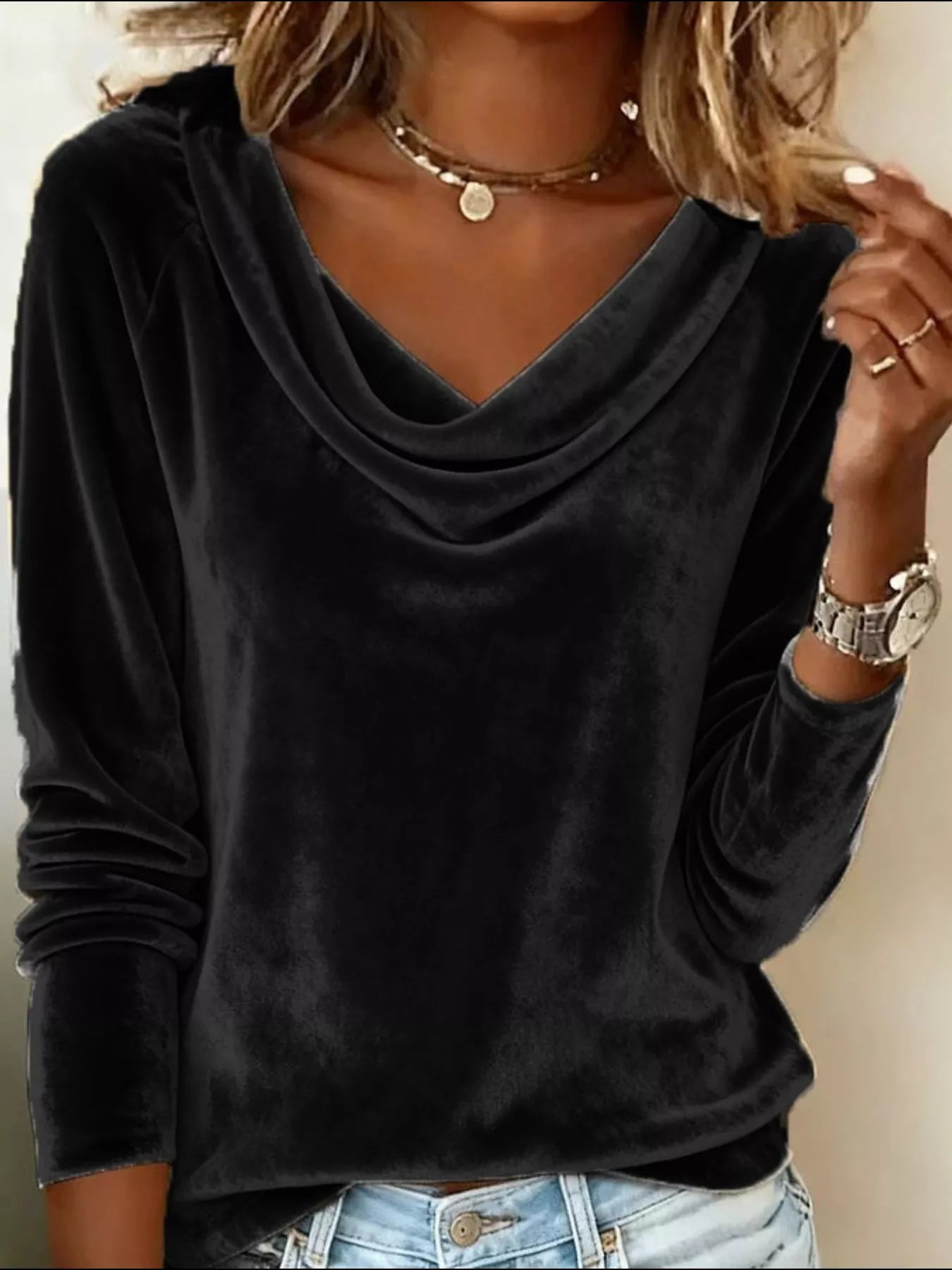 Person wearing a black long-sleeve top with a V-neckline, gold necklace, and watch on a neutral background.