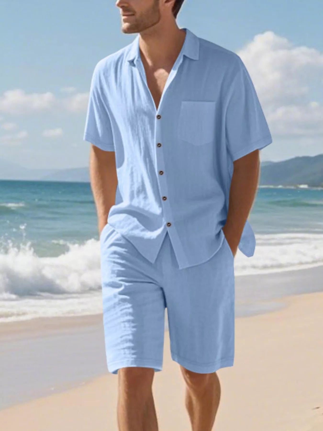 NEWYORKLISTED ATLAS MEN'S COLLECTION: Man wearing a light blue shirt and shorts set on a beach with ocean and sky in the background