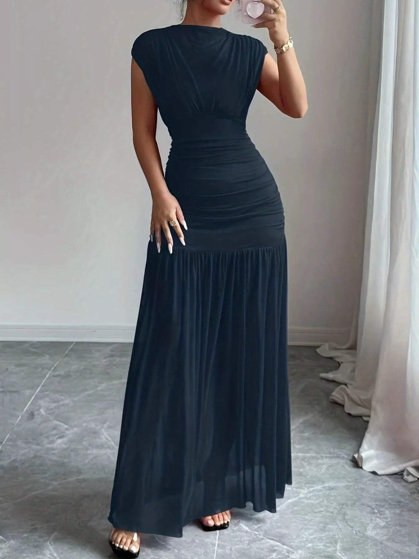 NEWYORKLISTED STYLE COLLECTION: Woman wearing a long black dress in a room with a neutral background