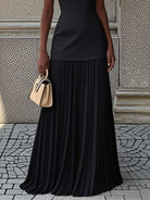 NEWYORKLISTED STYLE COLLECTION: Person wearing a black pleated skirt and holding a beige handbag against a textured wall.