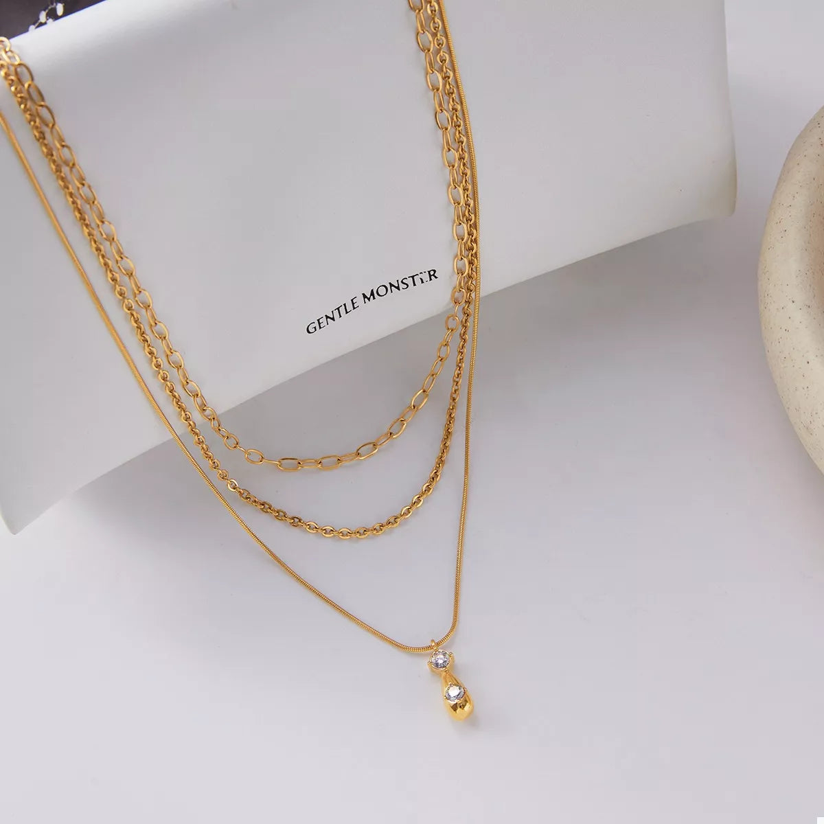 NYLD Glamour Collection by NEWYORKLISTED: Gold chain necklace with a small pendant on a white surface with 'GENTLE MONSTER' branding.