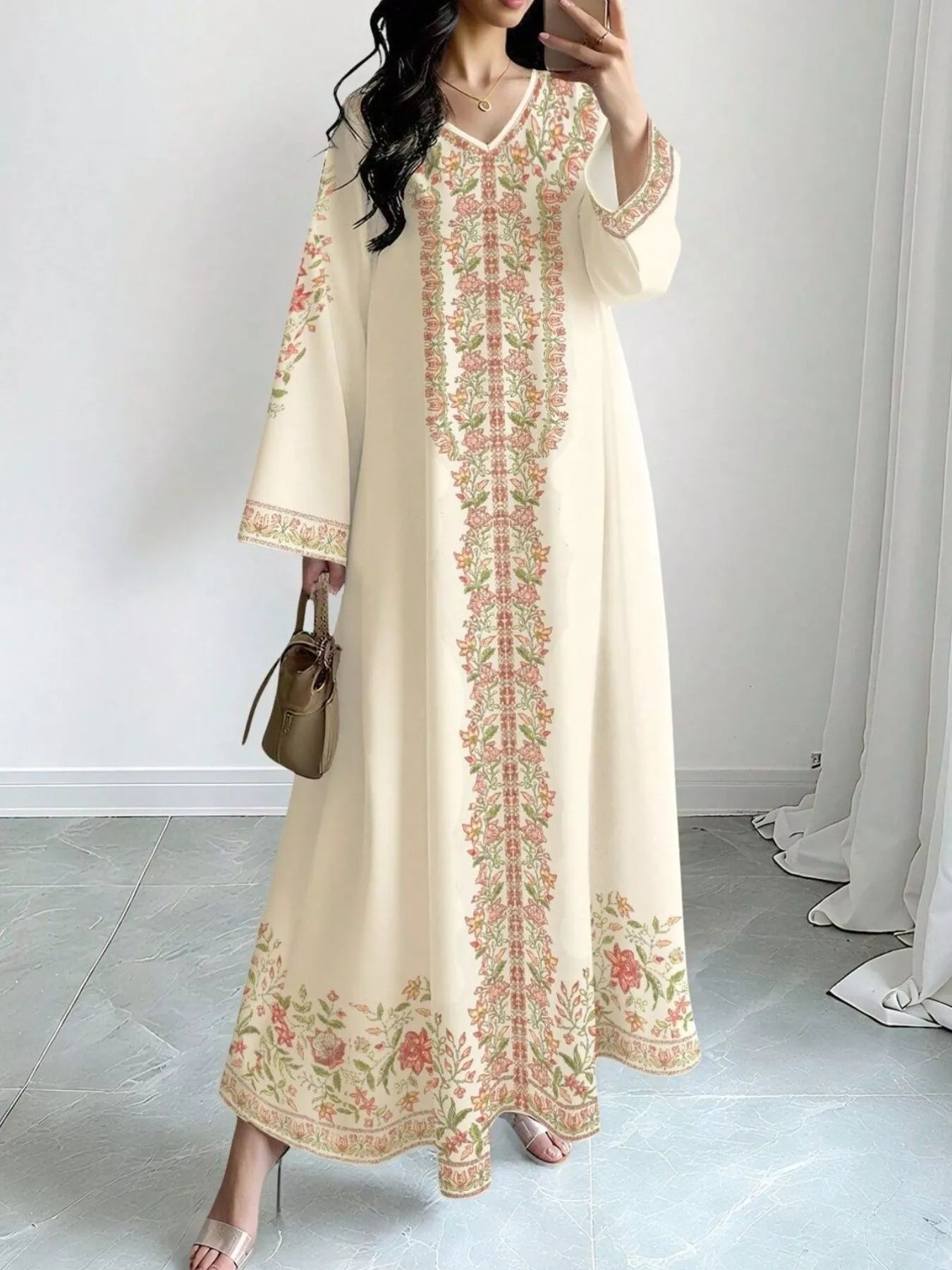 NEWYORKLISTED STYLE COLLECTION: Woman wearing a long, cream-colored dress with floral embroidery in a room with white walls and gray floor.