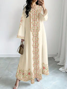 NEWYORKLISTED STYLE COLLECTION: Woman wearing a long, cream-colored dress with floral embroidery in a room with white walls and gray floor.