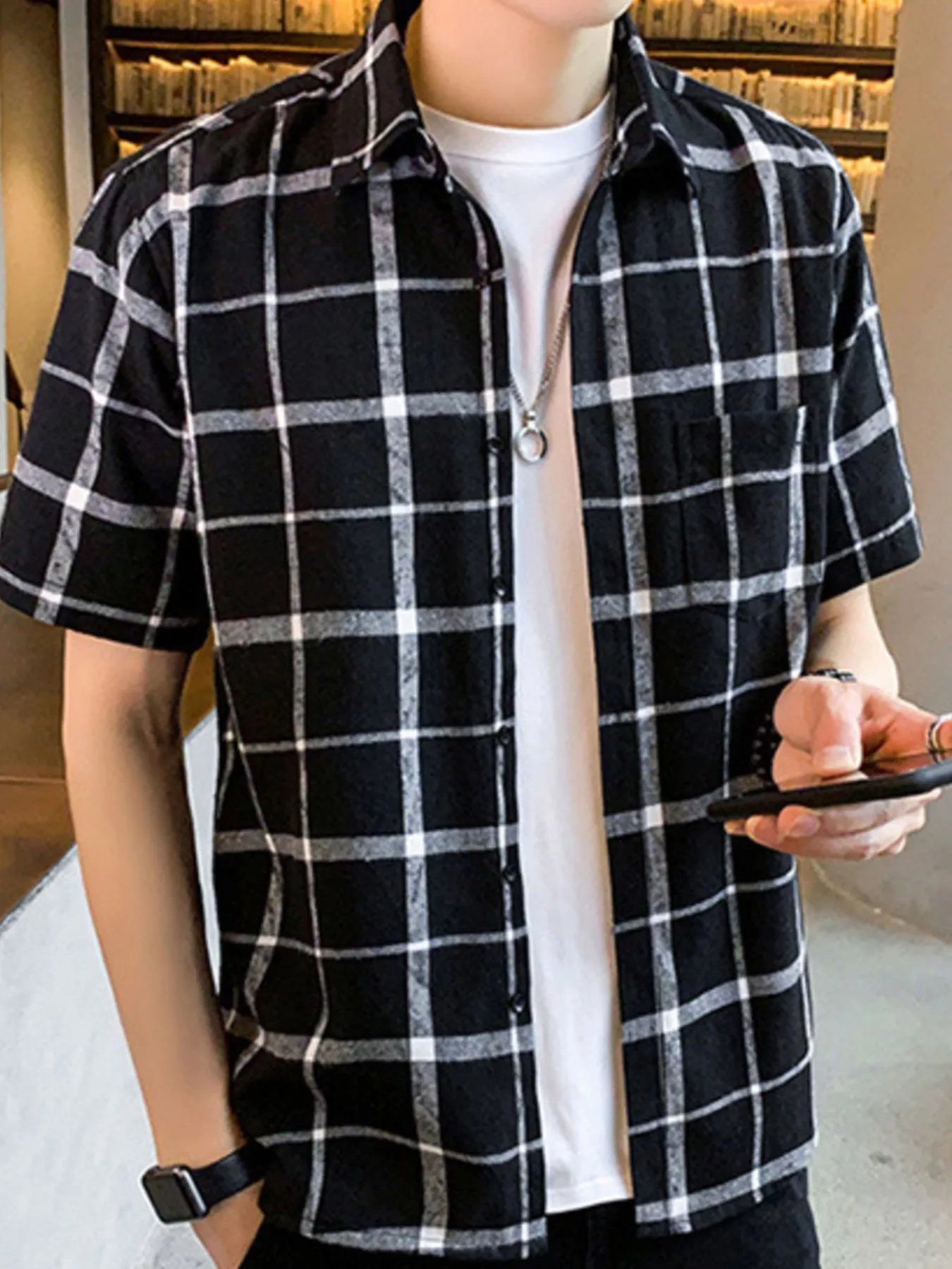NEWYORKLISTED ATLAS MEN'S COLLECTION: Person wearing a black and white checkered shirt over a white t-shirt, holding a phone.