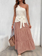 NEWYORKLISTED STYLE COLLECTION: Woman wearing a white top and patterned skirt with a straw bag against a light gray wall.