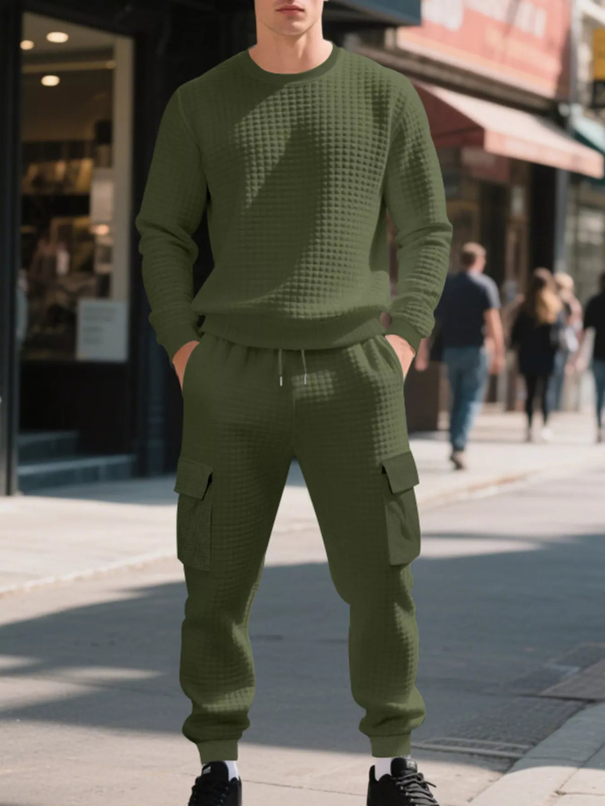 NEWYORKLISTED ATLAS MEN'S COLLECTION: A man wearing an olive green waffle-knit crewneck sweatshirt and matching cargo jogger pants, standing on a city sidewalk.