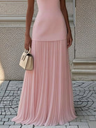 NEWYORKLISTED STYLE COLLECTION: Person wearing a pink pleated dress holding a beige handbag on a stone pavement.